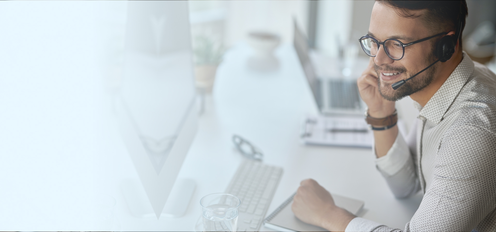 Man with glasses sitting at a desk talking into a headset.