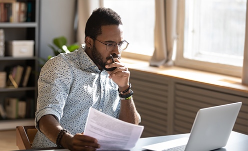 Man in glasses intensely analyzing his computer while holding papers.